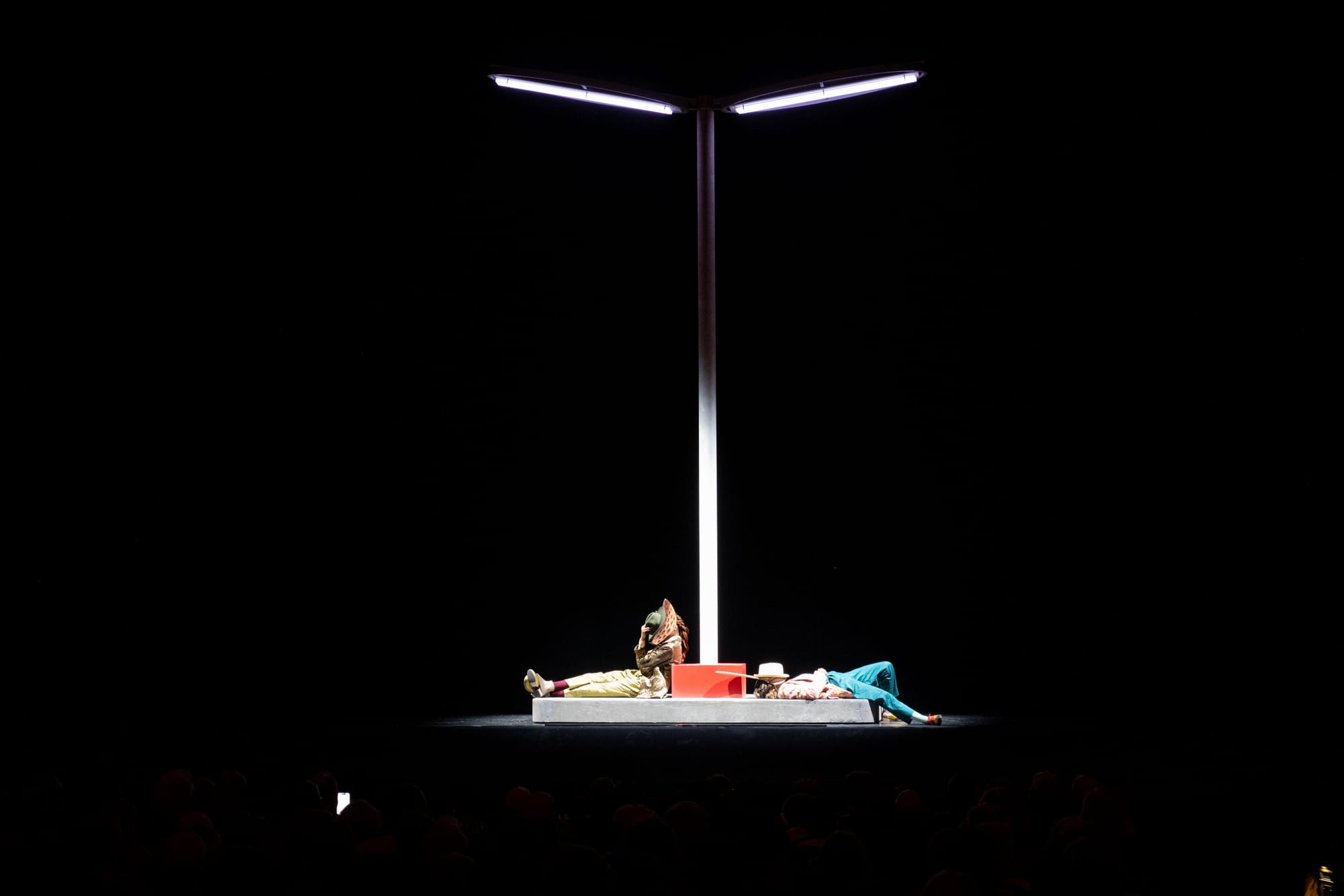 Two people in animal costumes sat under a streetlight on a stage in an auditorium.