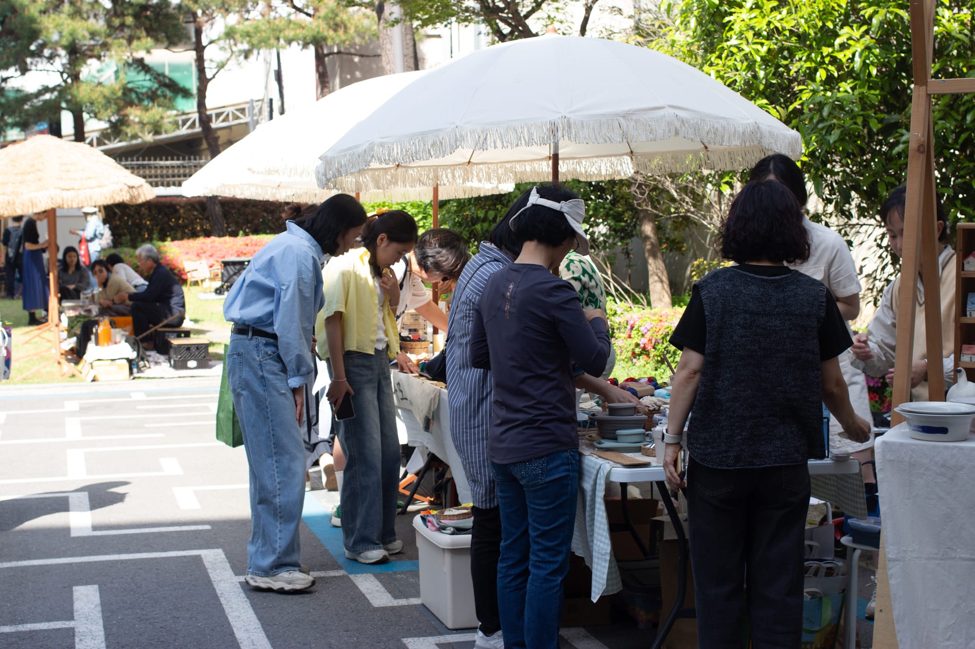 An outdoor market, with a handful of customers perusing the tables and white umbrellas providing shade.