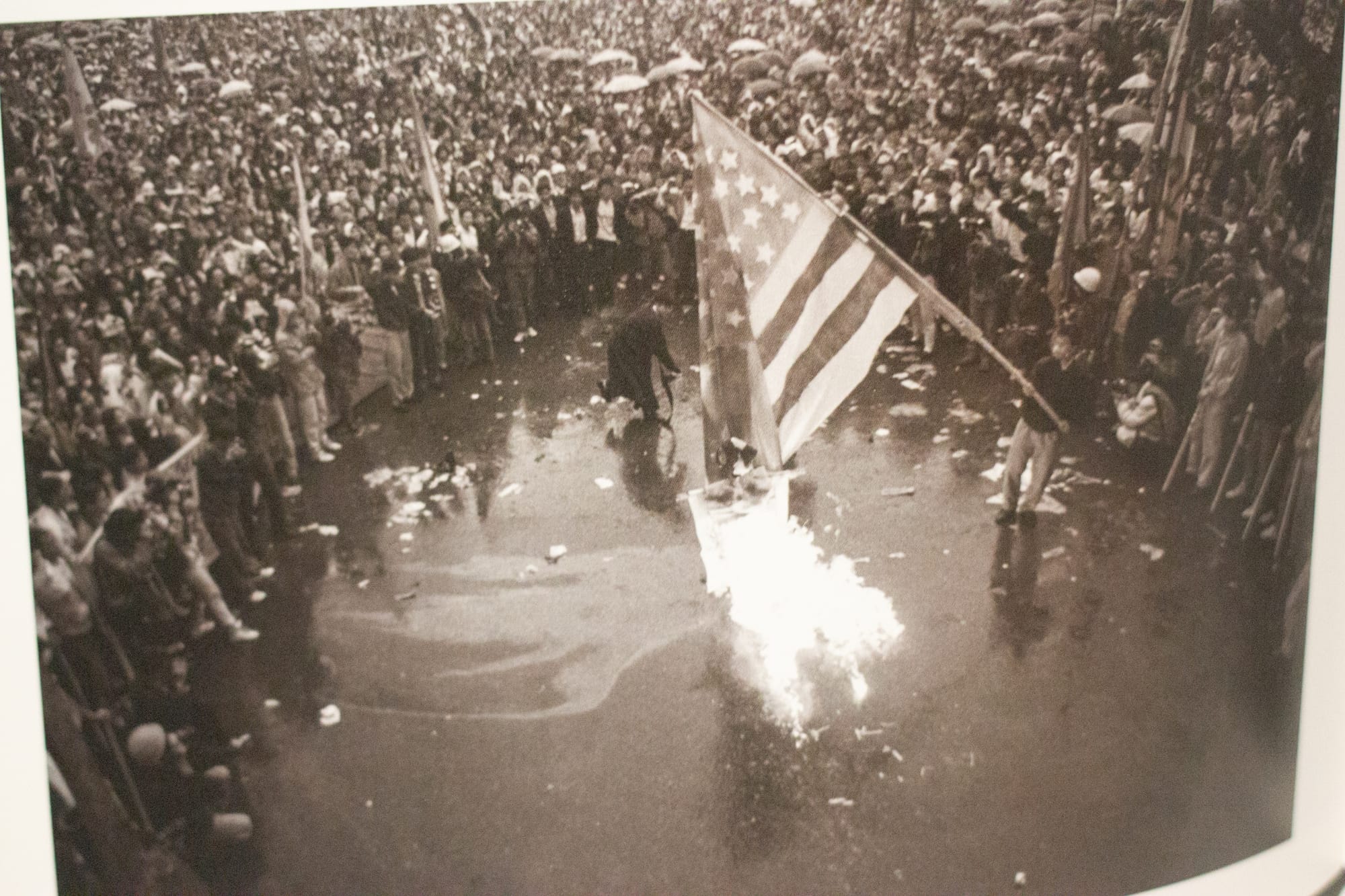 A huge crowd forms in a circle. At the center is a handmade American flag being burned.