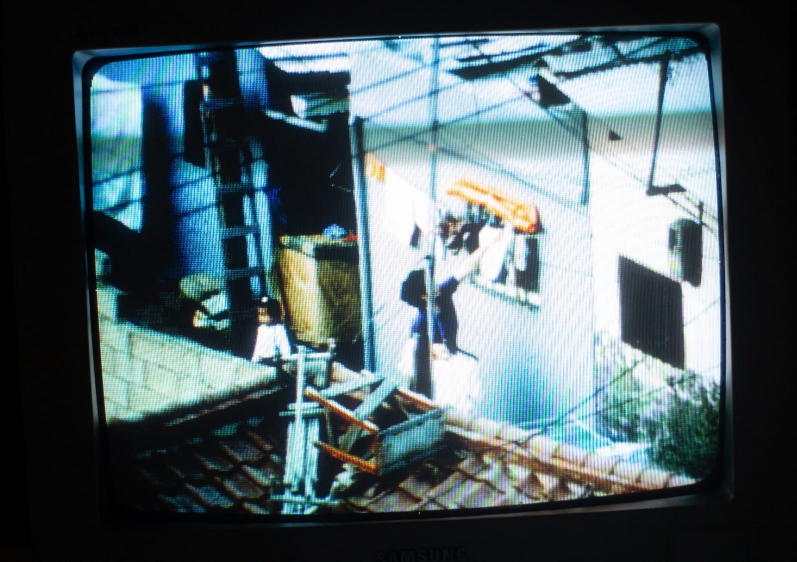 A fuzzy CRT television playing a richly colored movie. It shows an outdoor scene in an alley between houses.