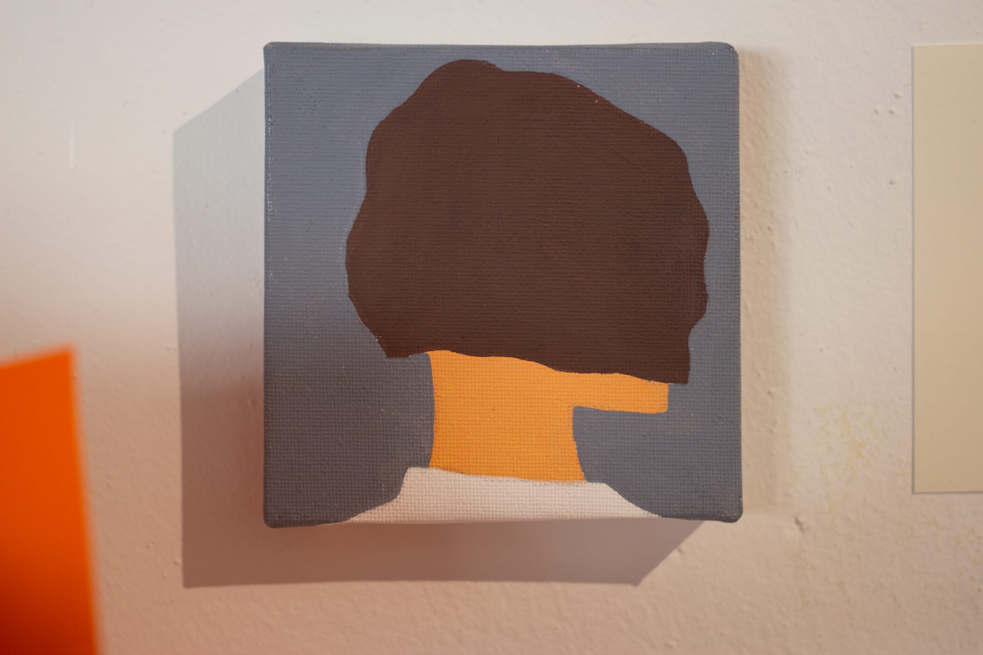 A small square painting shows the head and neck of a figure facing away from the viewer. The colors are muted and simple.