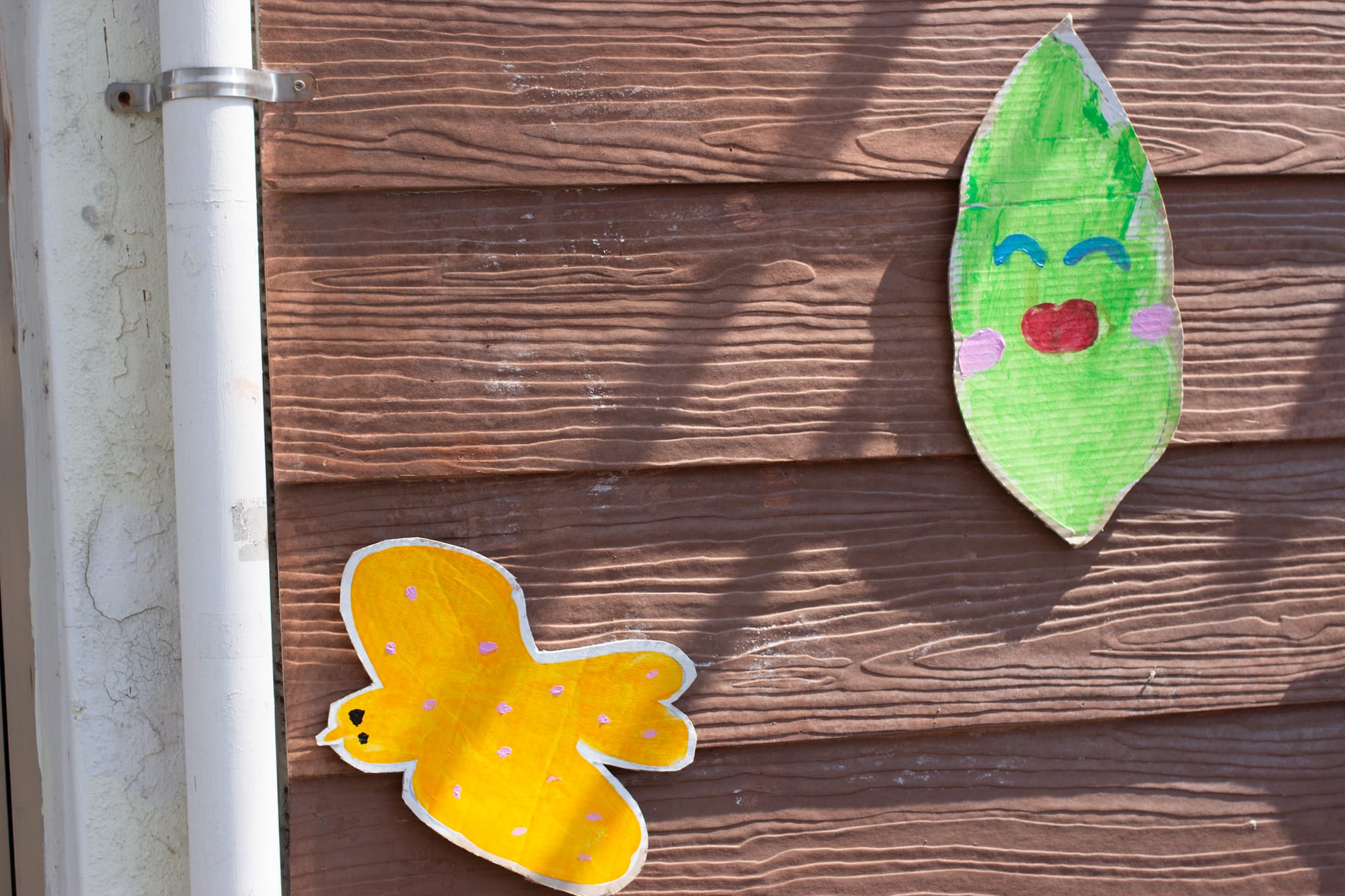 Two cut-out drawings are on an exterior wall. One is a curvy yellow bird. The other is a smiling leaf.