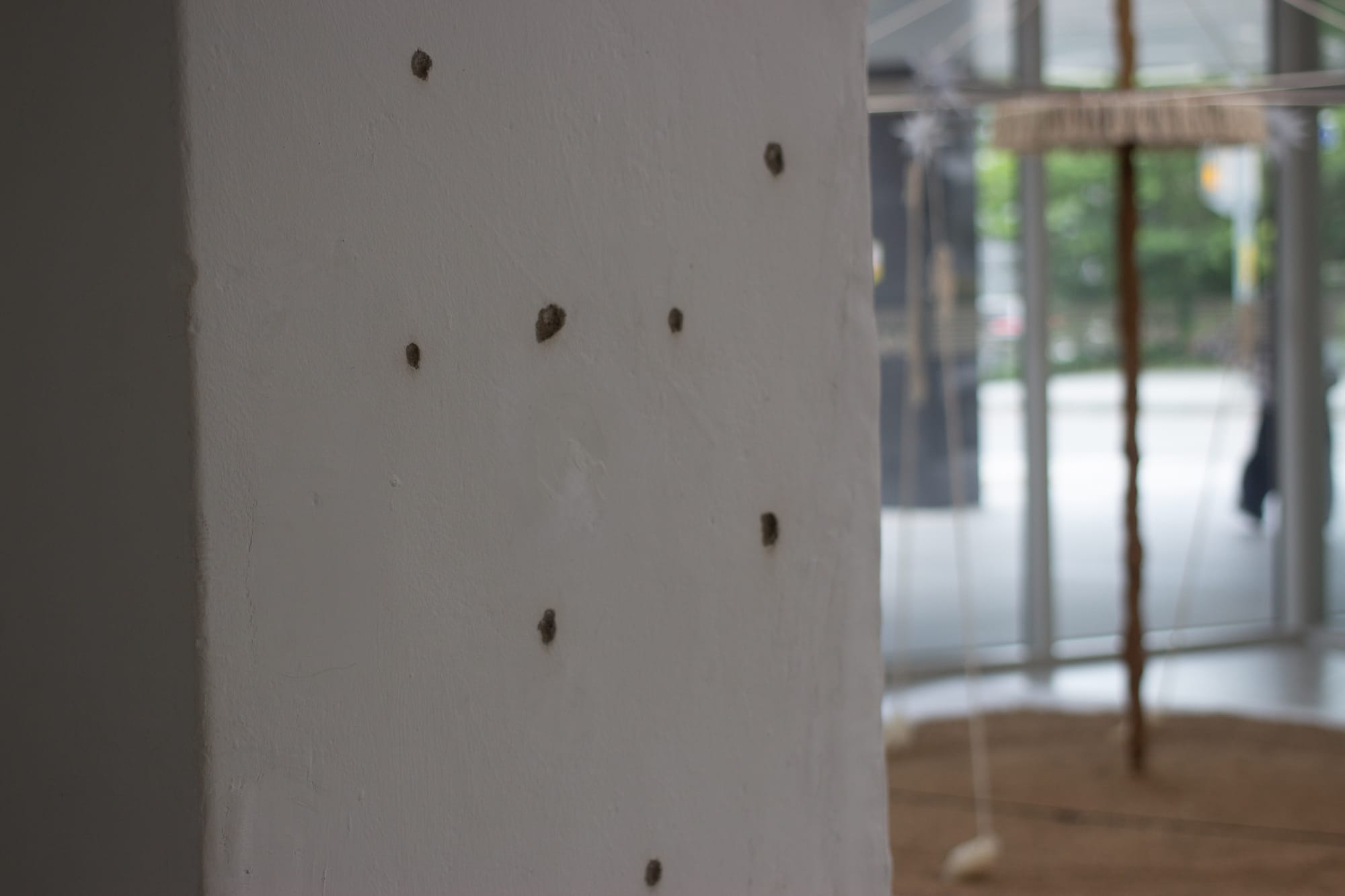 In the foreground, a white rectangular pillar with several bullet holes. The six-hand installation is blurry in the background.