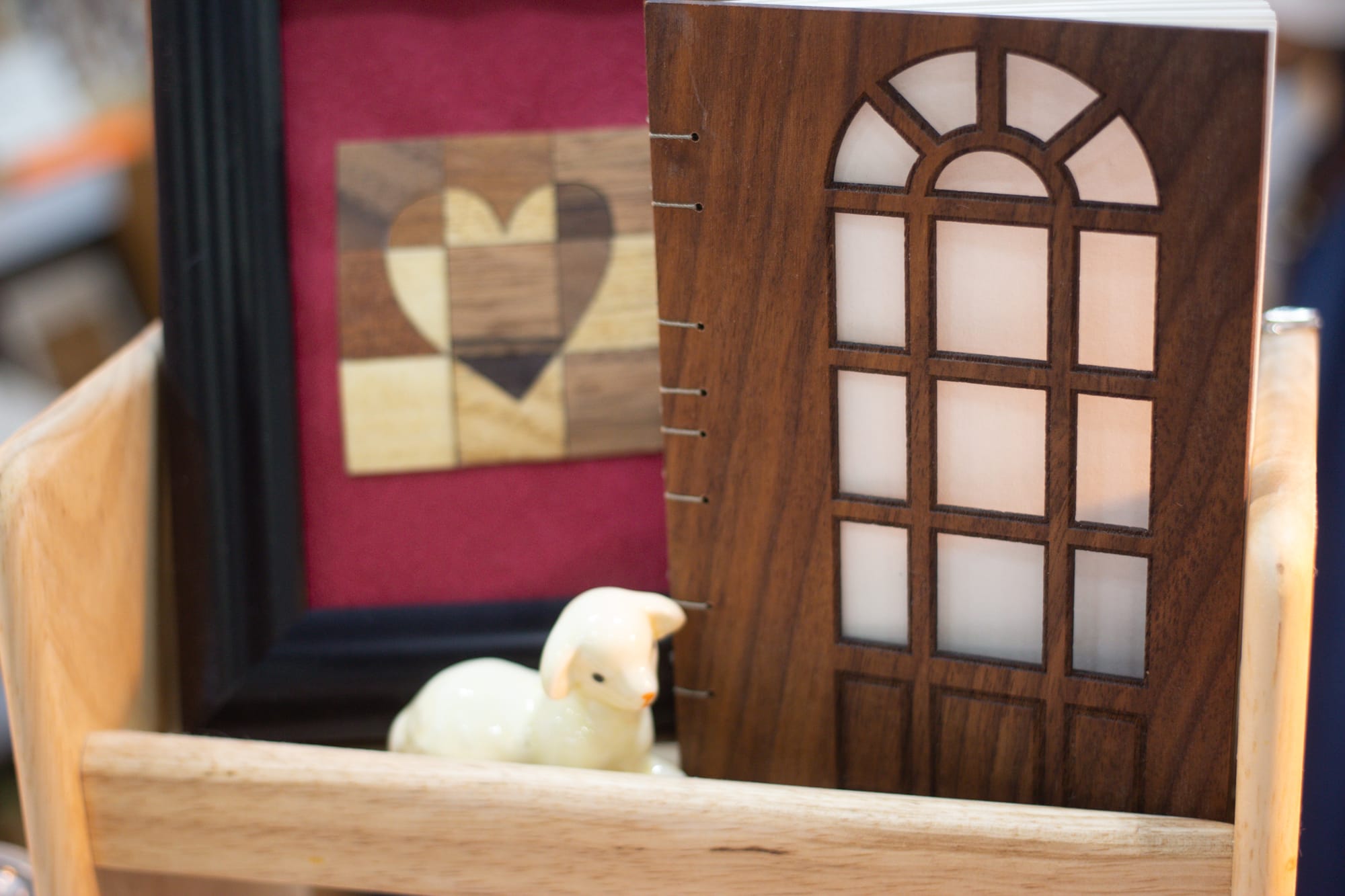 A miniature sculpture of a lamb, a notebook with a wooden cutout door as a cover, and a framed wooden collage in the shape of a heart.