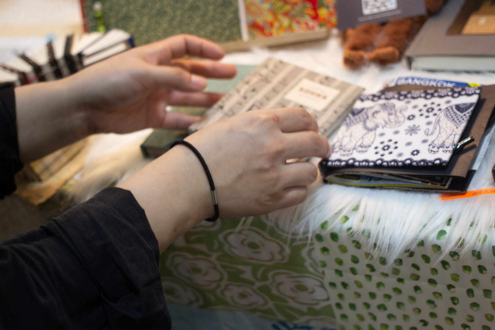 Two hands touch a few handmade books on a table. The books are filled with a variety of paper.