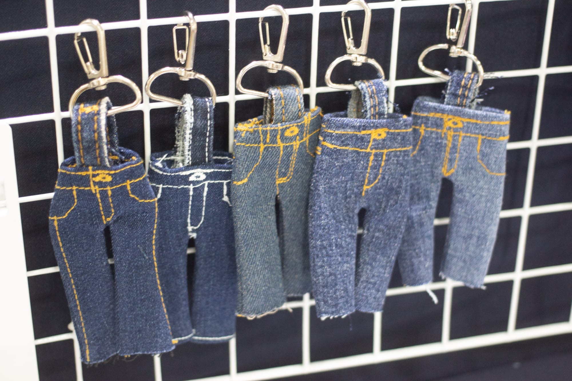 Five keychains made of denim, in the shape of tiny pairs of jeans with yellow thread "seams."
