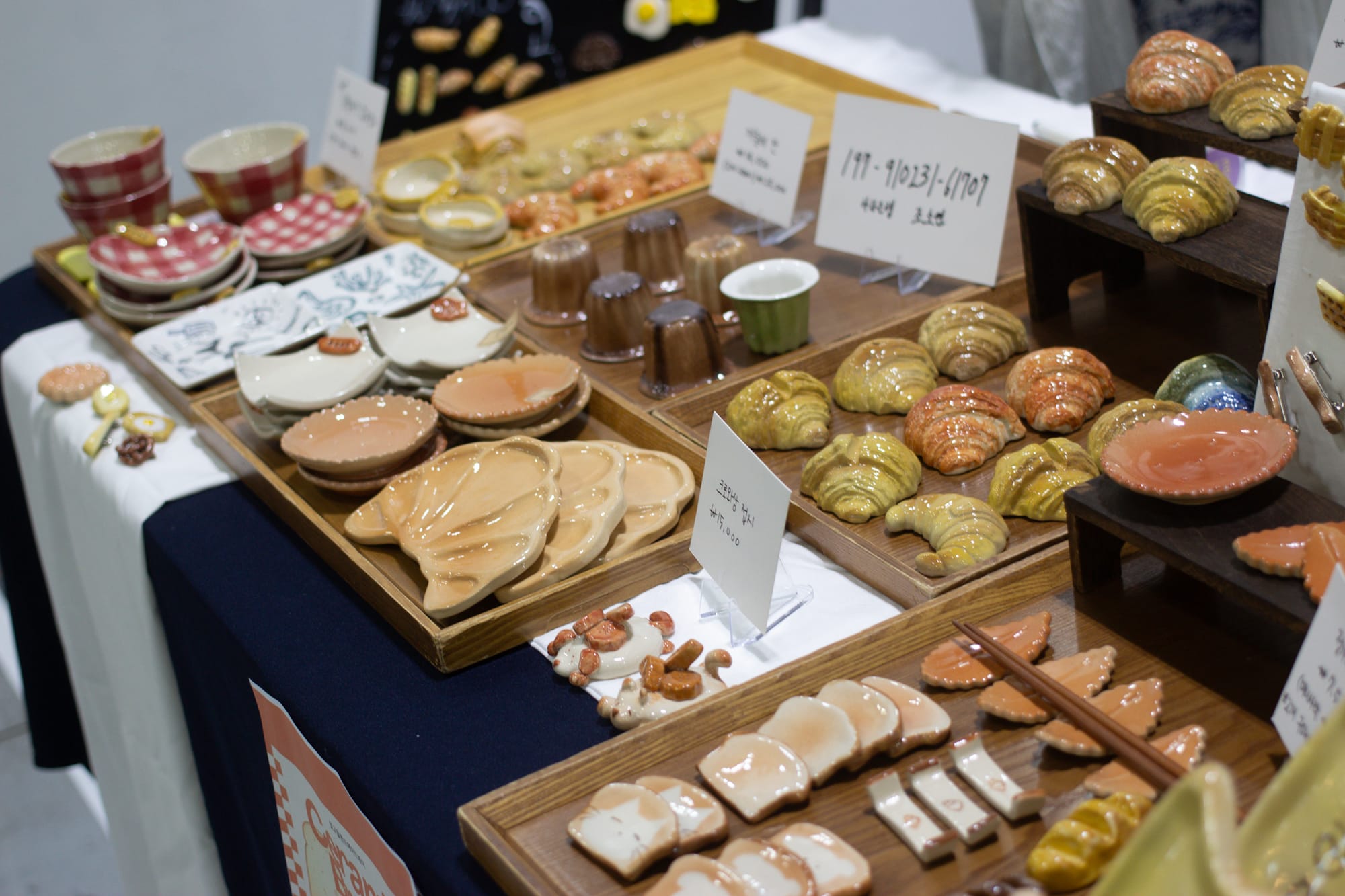 A display of shiny ceramics that look like croissants, toast, puddings and other baked goods.