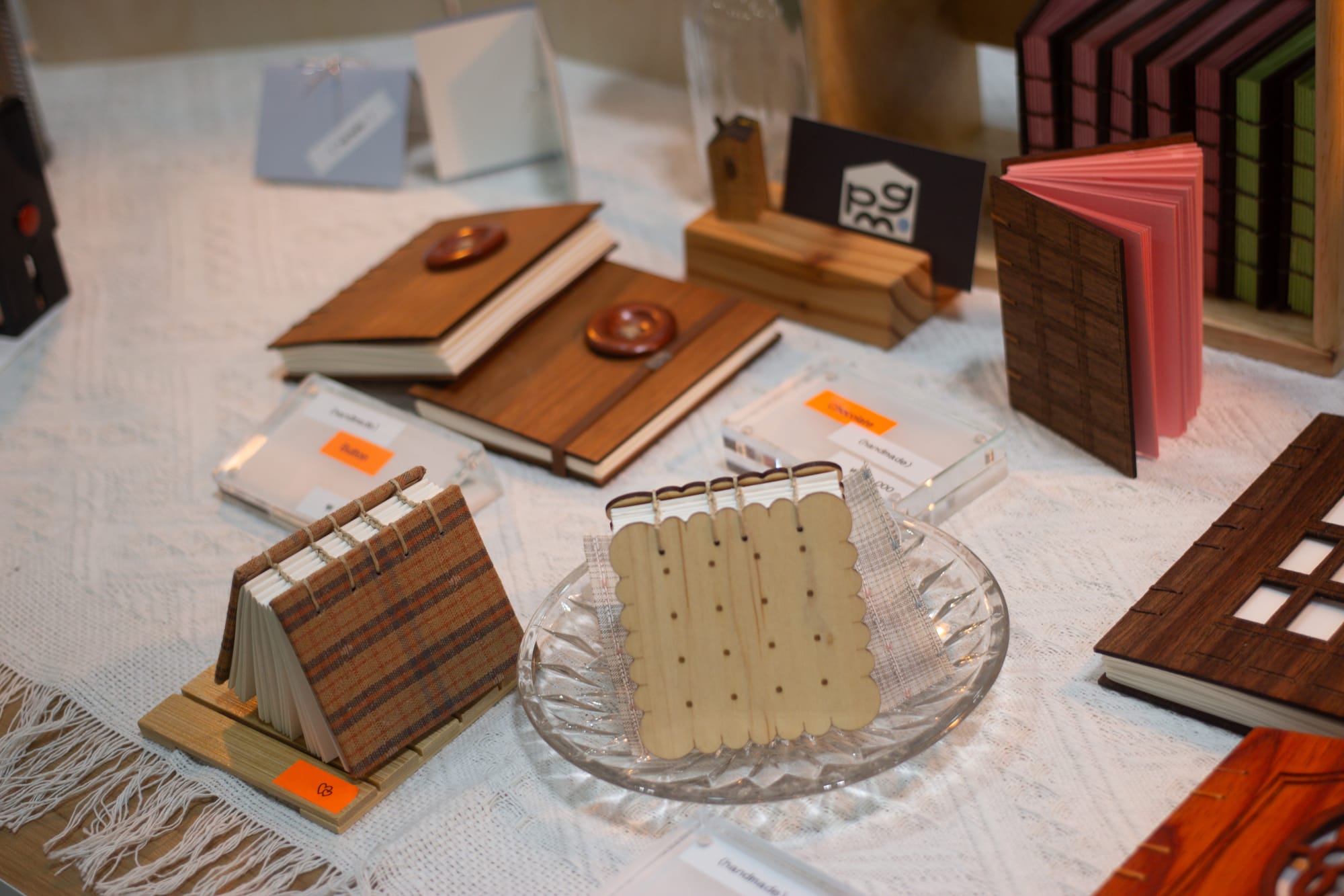 Display of miniature books on a table with a white tablecloth. One of the books, with a wooden light beige cover, is in the shape of a square cracker.