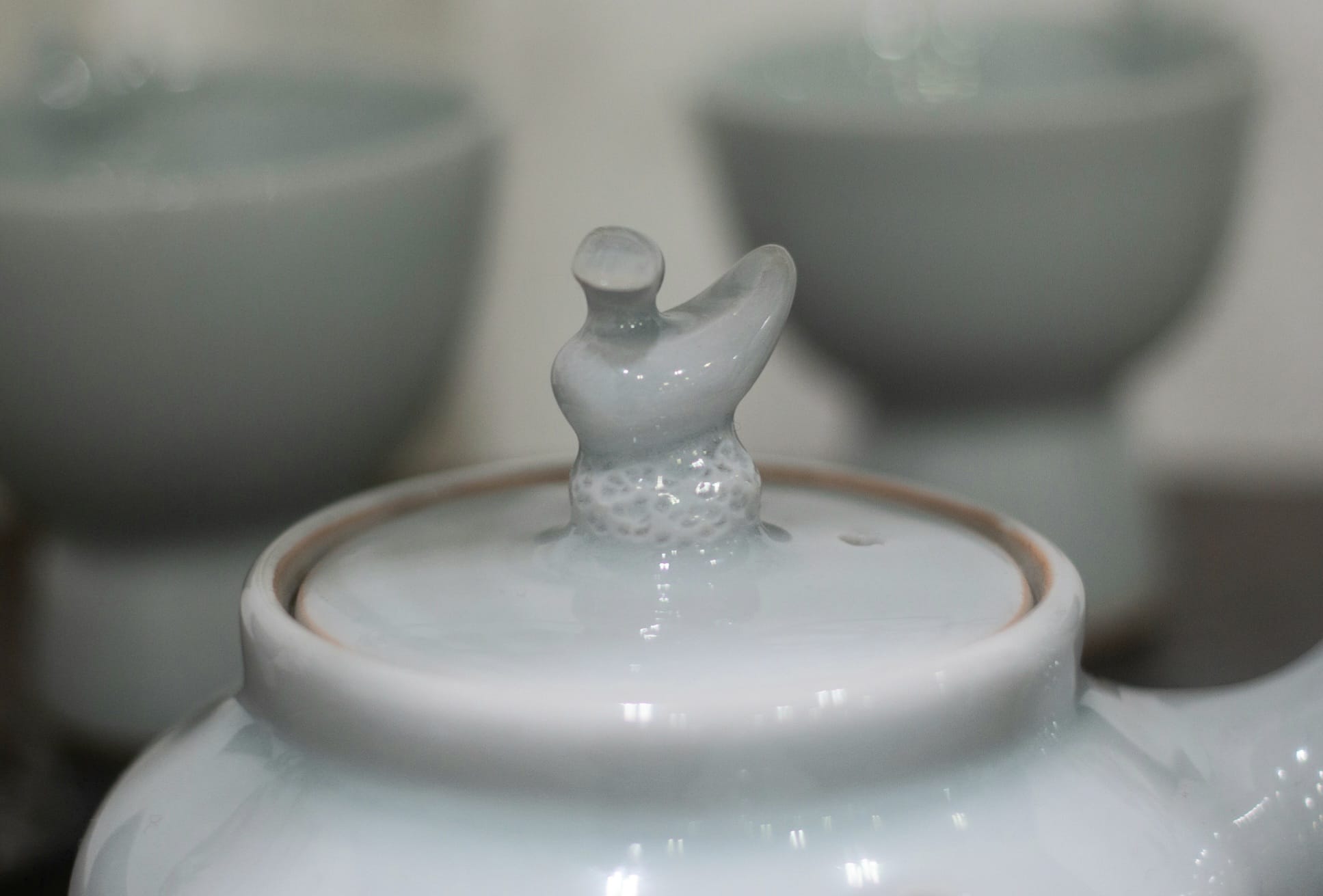 An abstract duck shape on the lid of a light green ceramic tea kettle.