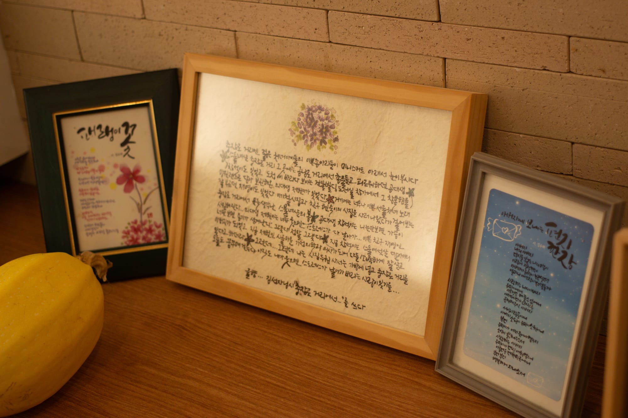 Three poems in Korean, in frames, sit on a shelf by a yellow melon.