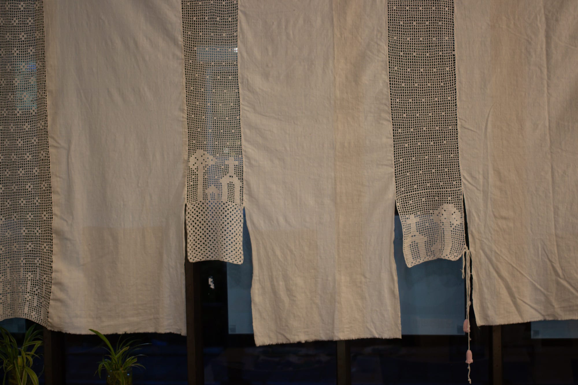 A white curtain split into sections of varying lengths. Alternating sections are lace, with images of buildings and trees.