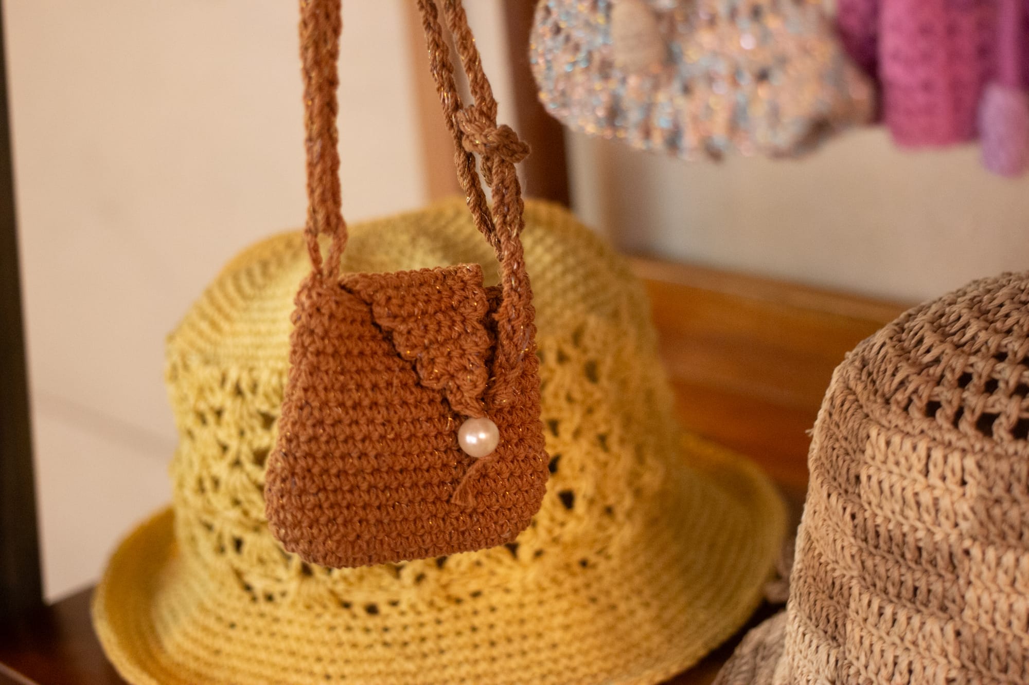 A small brown bag, knitted or crocheted, hangs in front of a yellow hat and a checkerboard brown and beige hat.