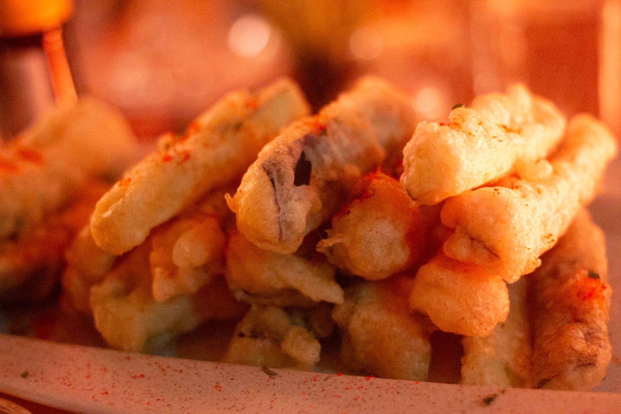 A warmly lit close-up photo of a pile of crispy battered eggplant sticks on a speckled plate.