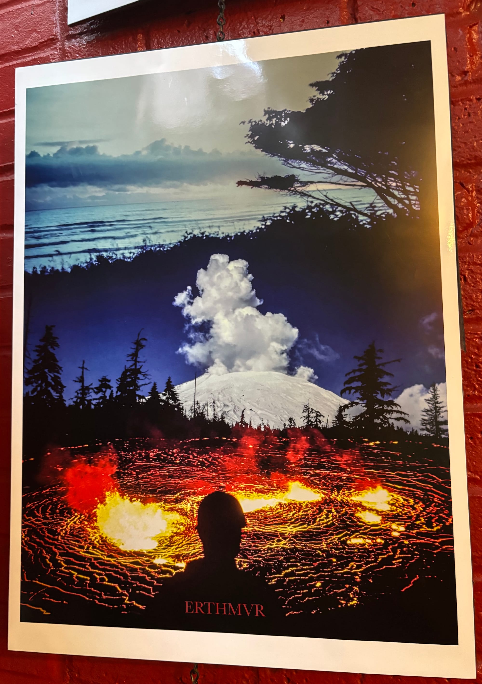 Artwork of a shadowy figure overlooking lava, a forest, mountains, and a shore.