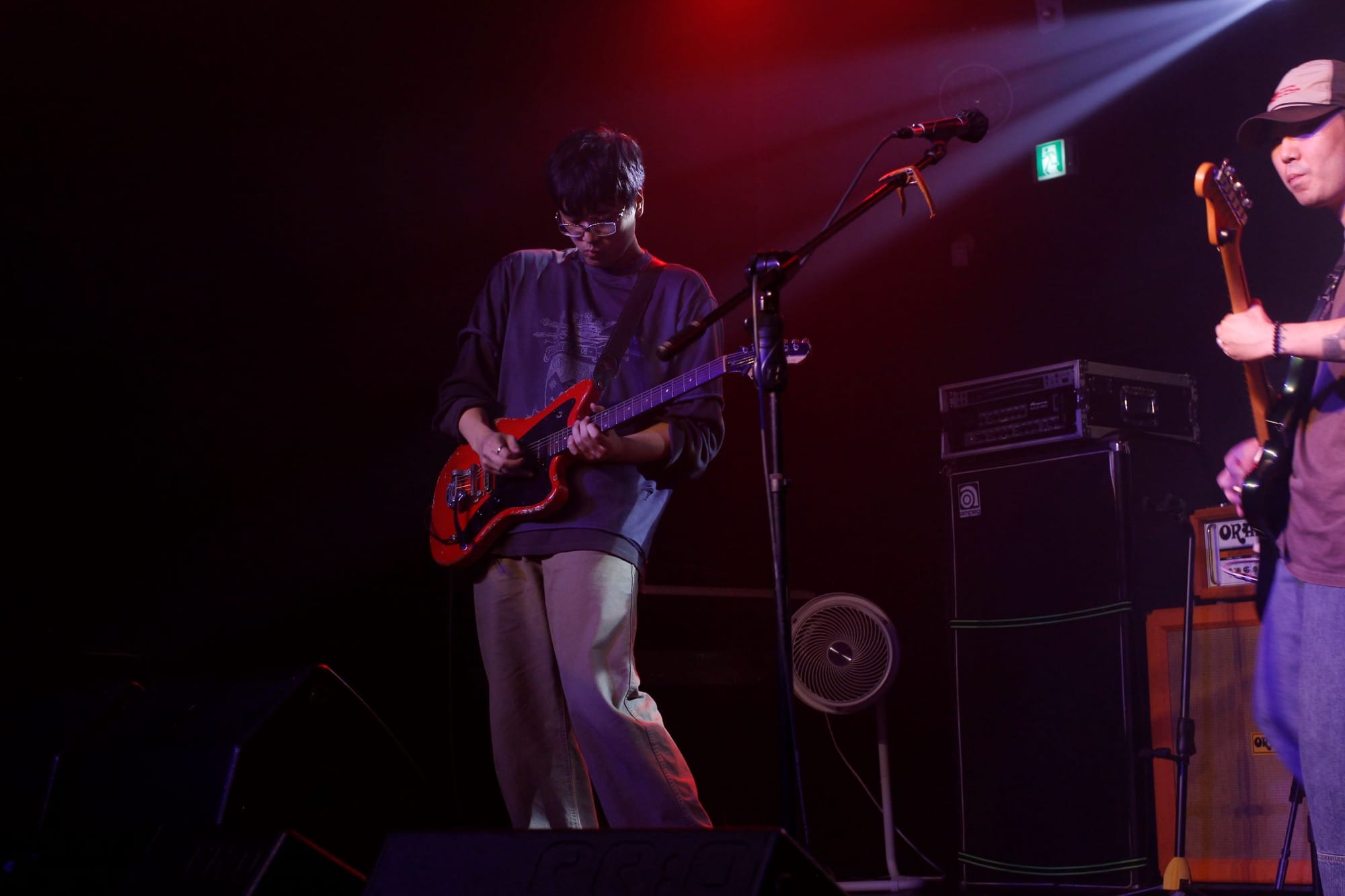 Im Chihyeon leans forward while playing guitar. The stage lights illuminate him from behind.