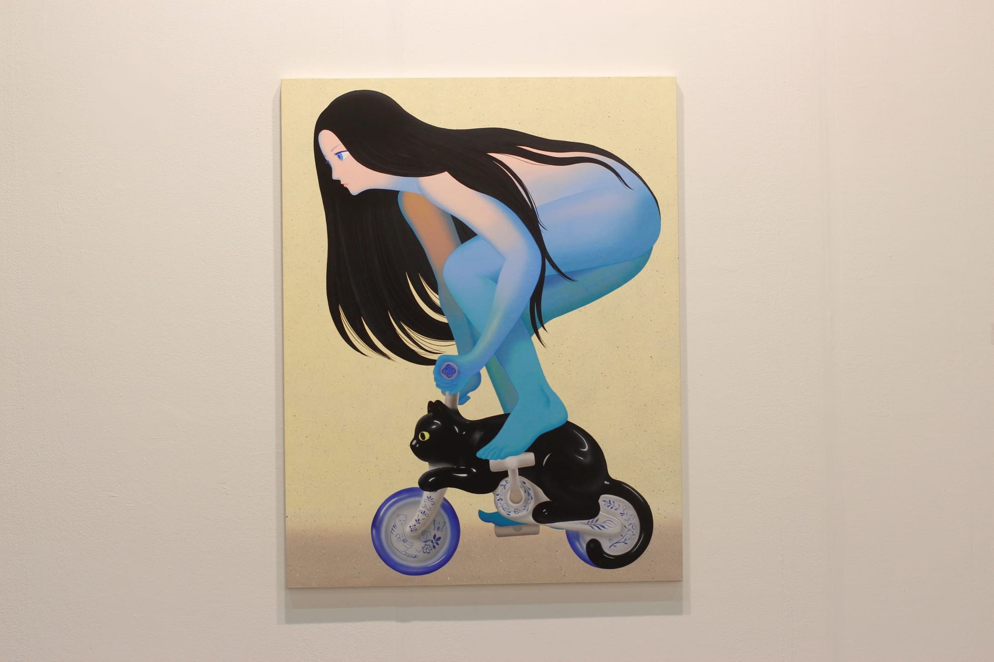 A person crouches to ride a tiny bicycle with an ultra-smooth and shiny black cat.