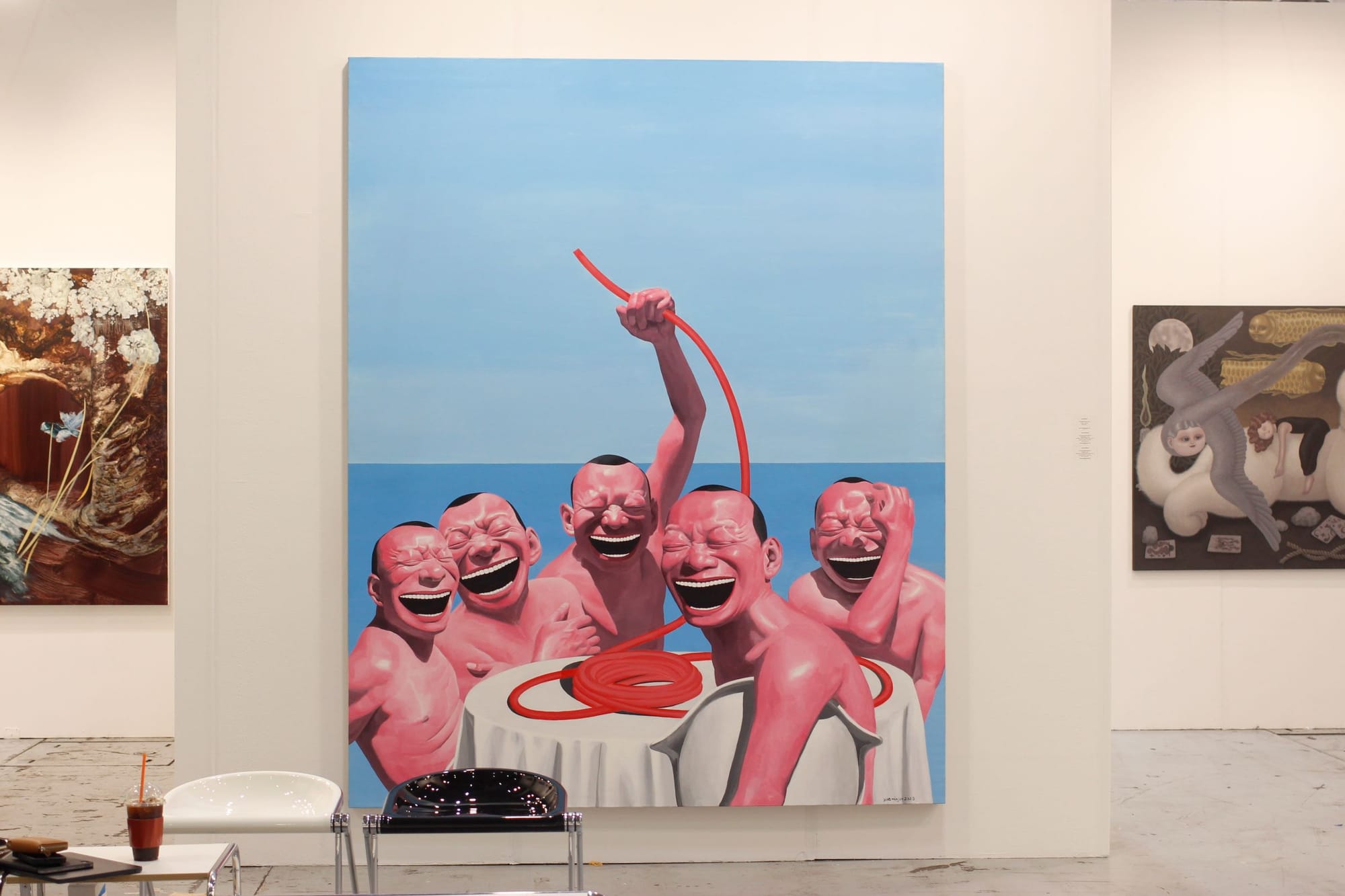 5 identical men with huge laughing mouths sit around a white table and coiled red pipe.