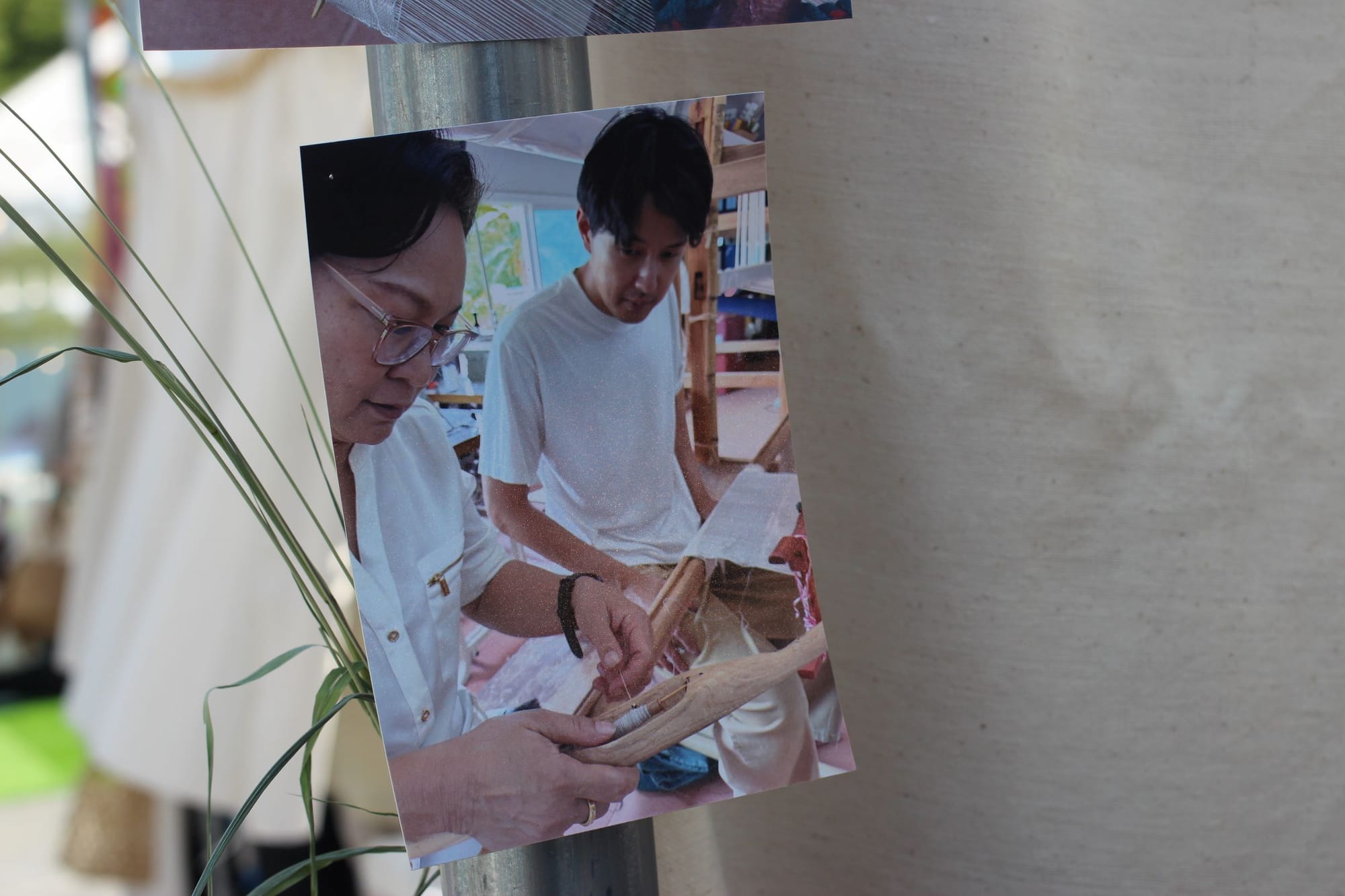 A photograph of two artisans working on textile art. Behind the pgoto is a green plant.