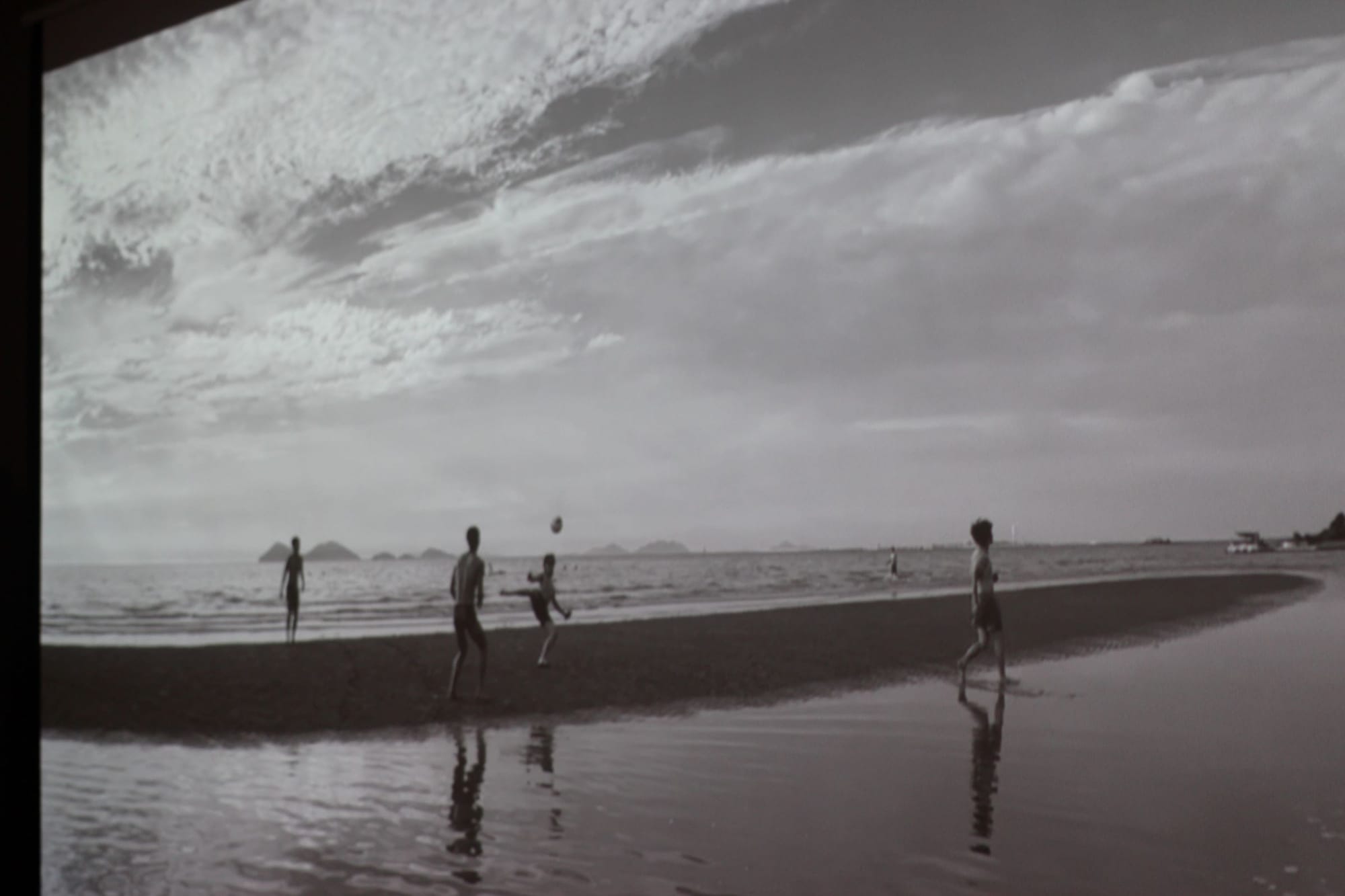 Black and white film still of four friends playing with a ball on a beach.