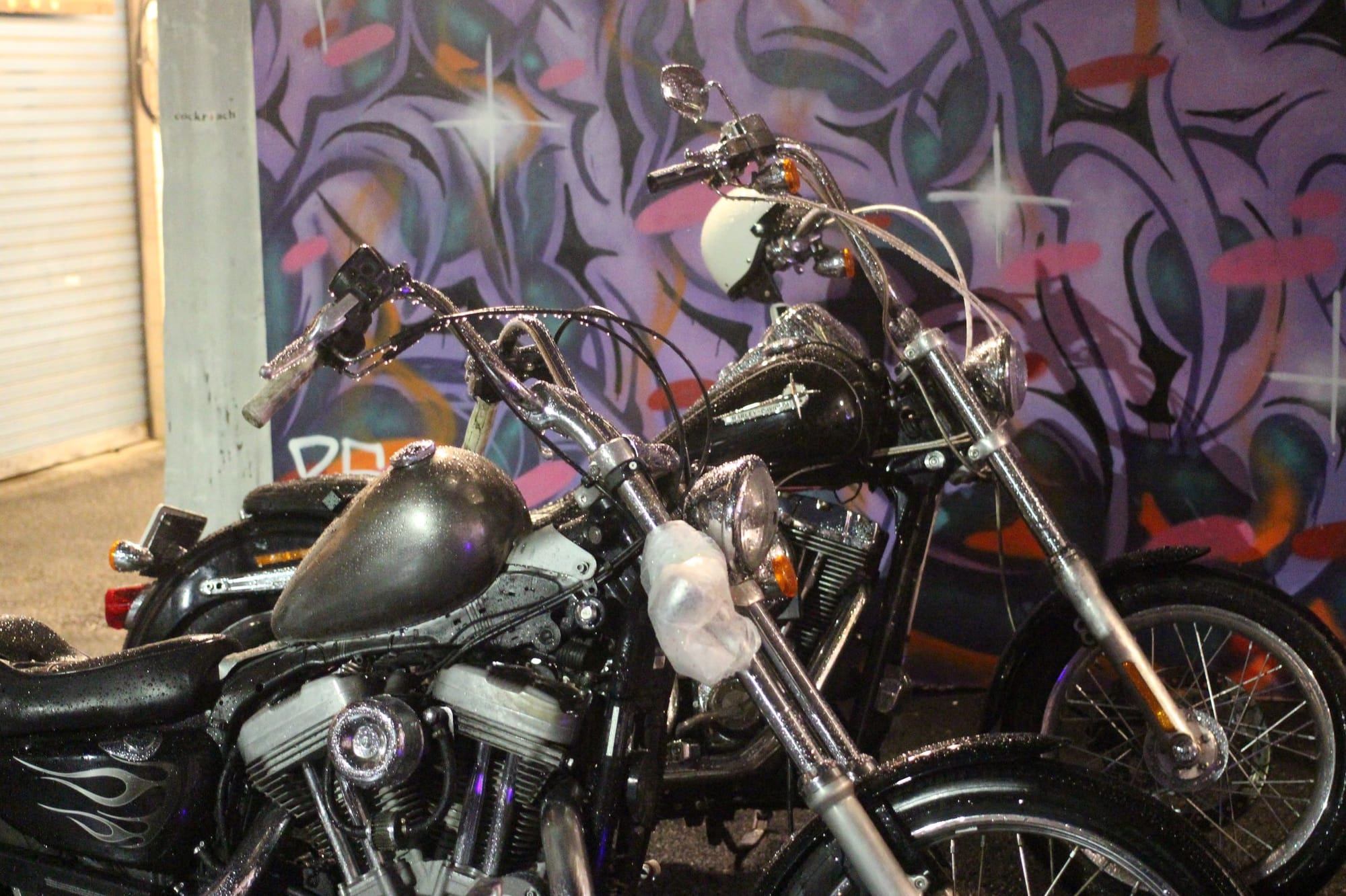 Two big, shiny motorcycles in front of a purple spray painted mural with shiny light details.