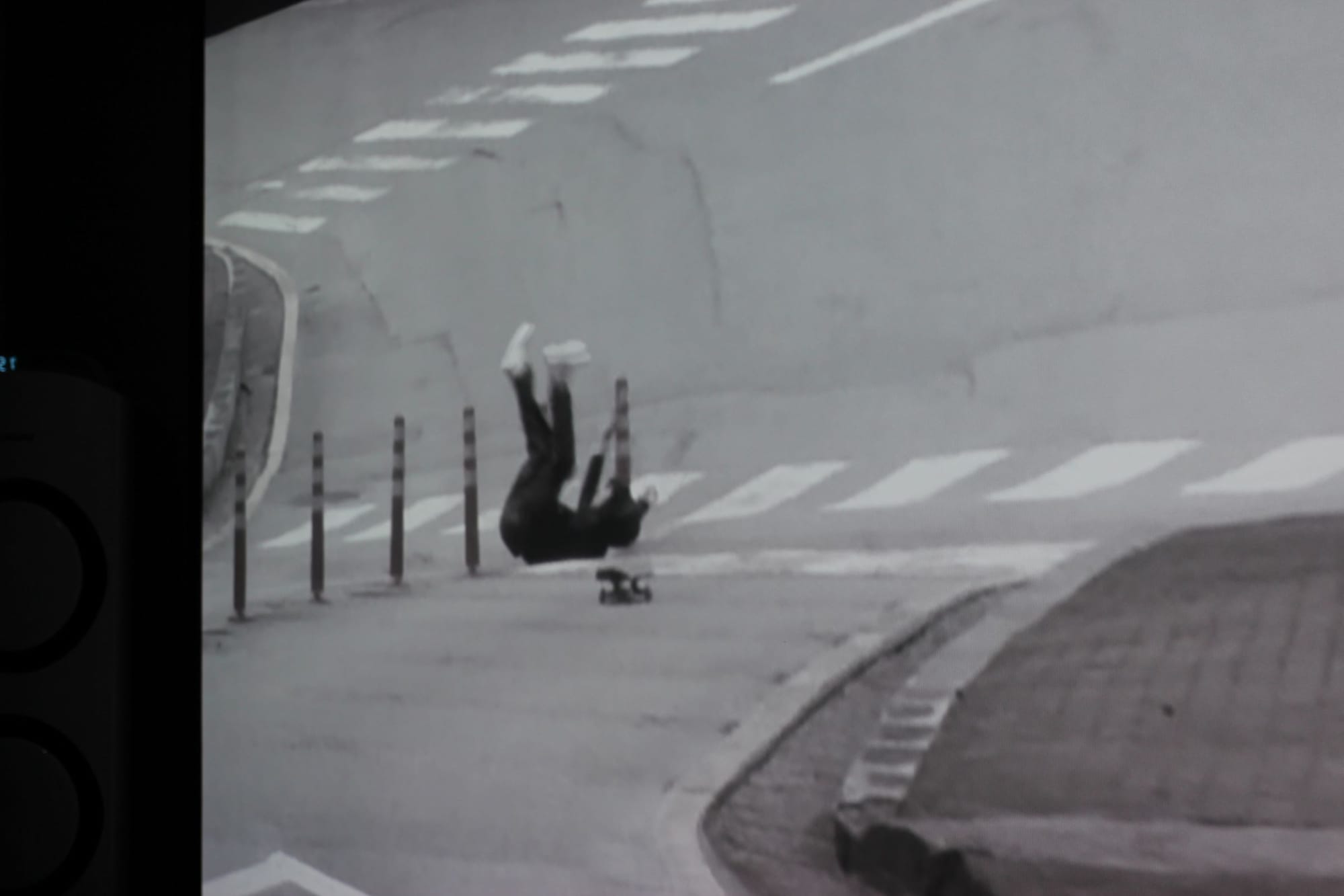 Black-and-white film still of a person falling off a skateboard, legs in the air like a dead cockroach.