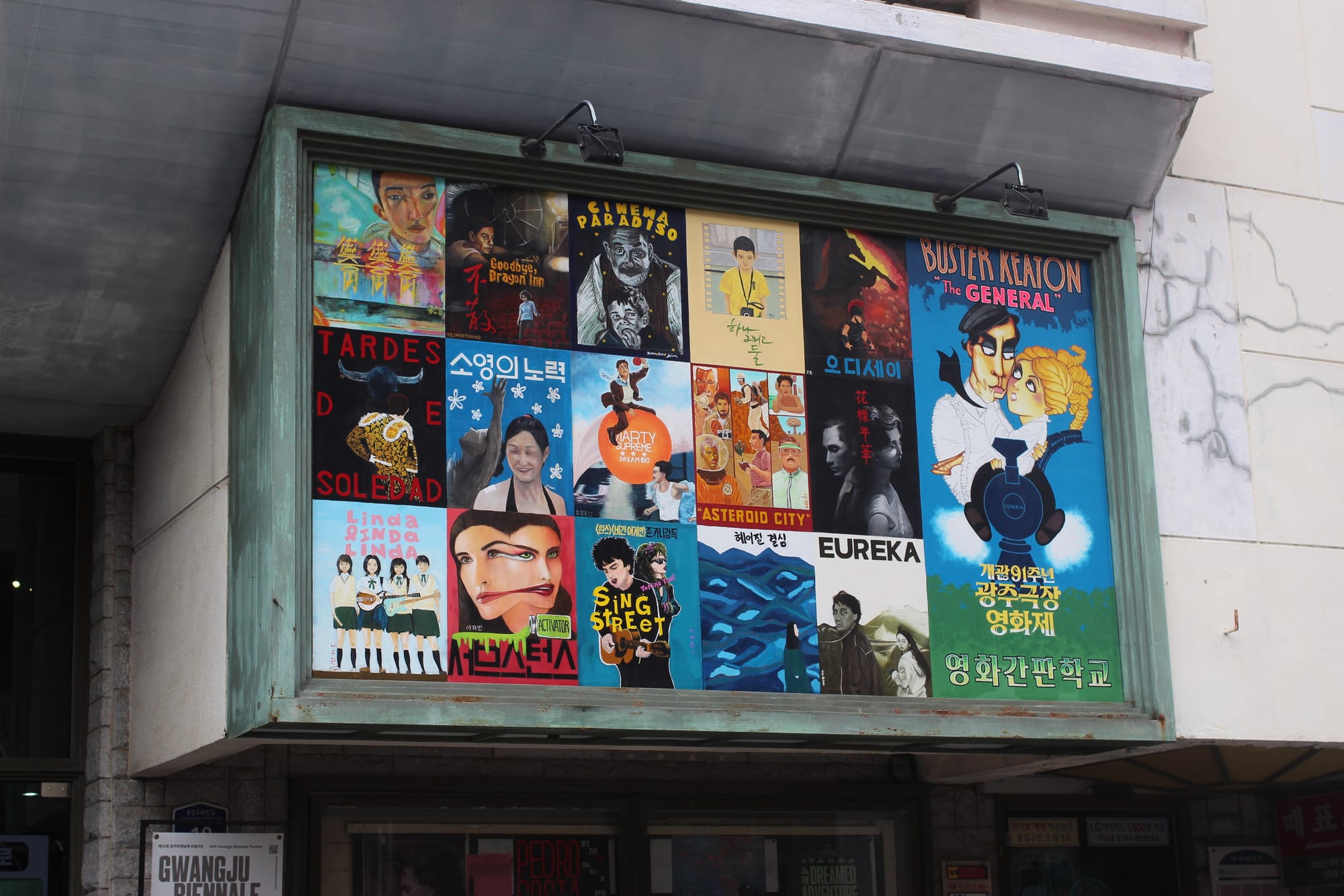 A building with retro mod architecture, featuring a large rectangular billboard-like composite painting with 16 movie posters.