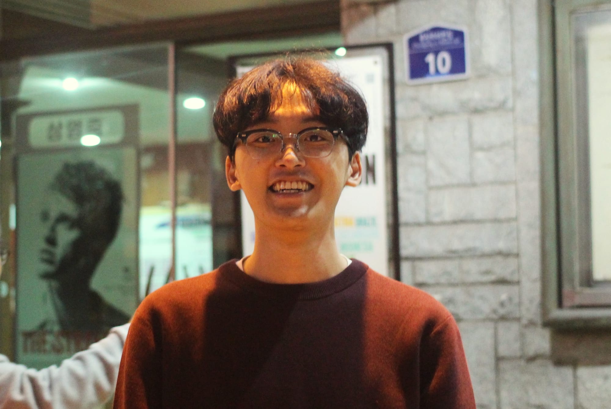 Kim Kyeong-Yong, in a maroon sweater, smiles in front of a movie theater.