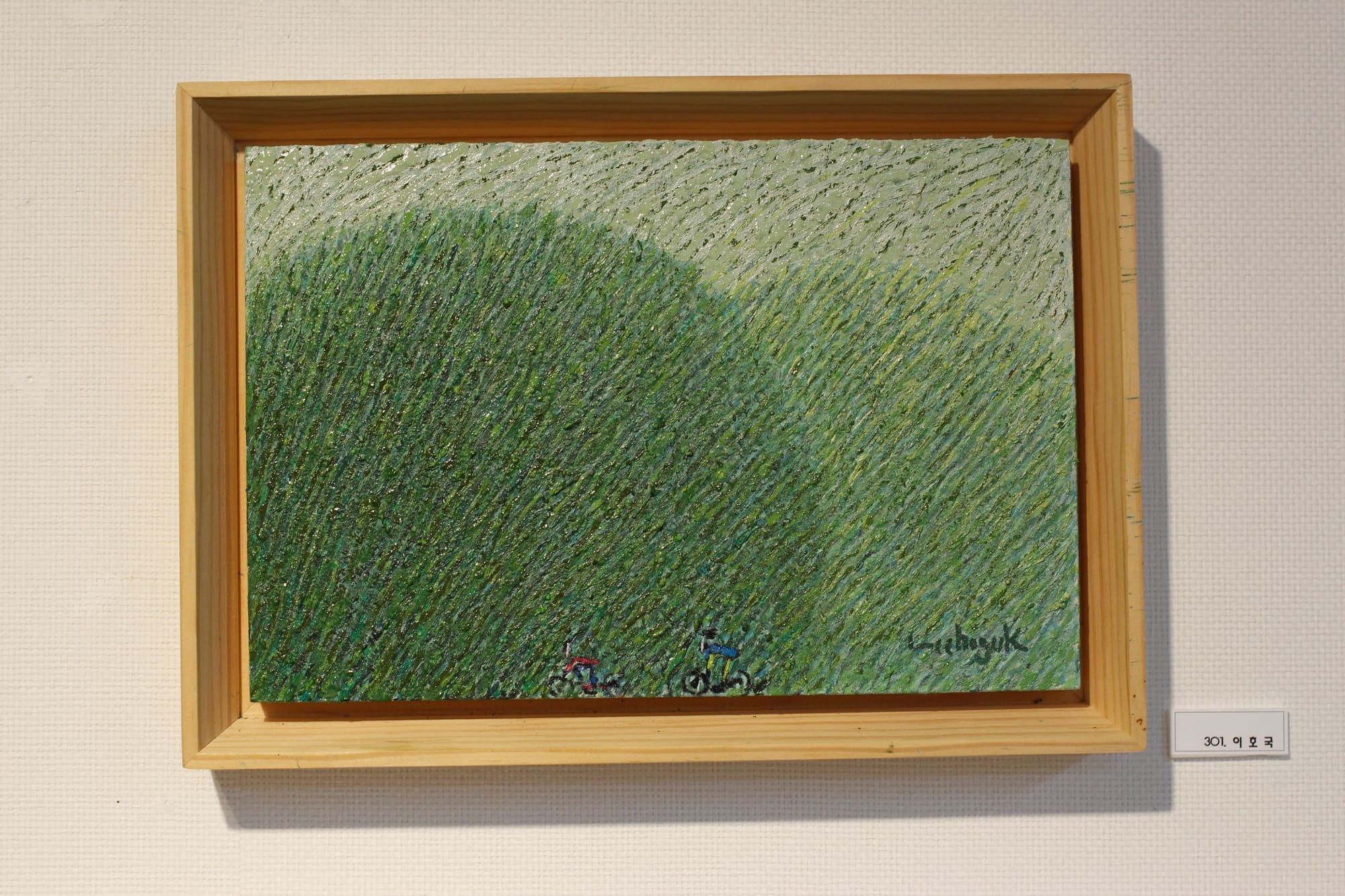 A textured painting of two large, round, green hills and two people on bikes, barely visible, at the bottom, quite small.