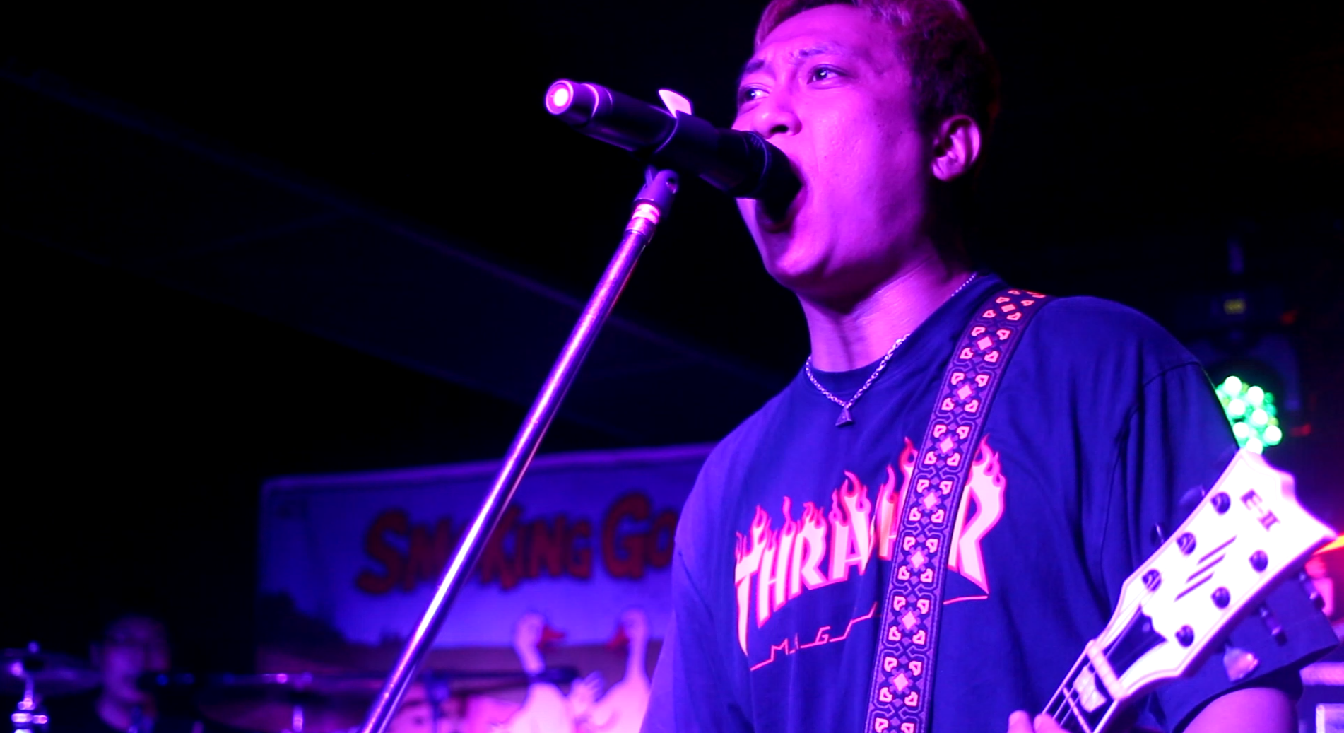 Smoking Goose singer wearing a Thrasher shirt sings into the mic and holds a guitar.