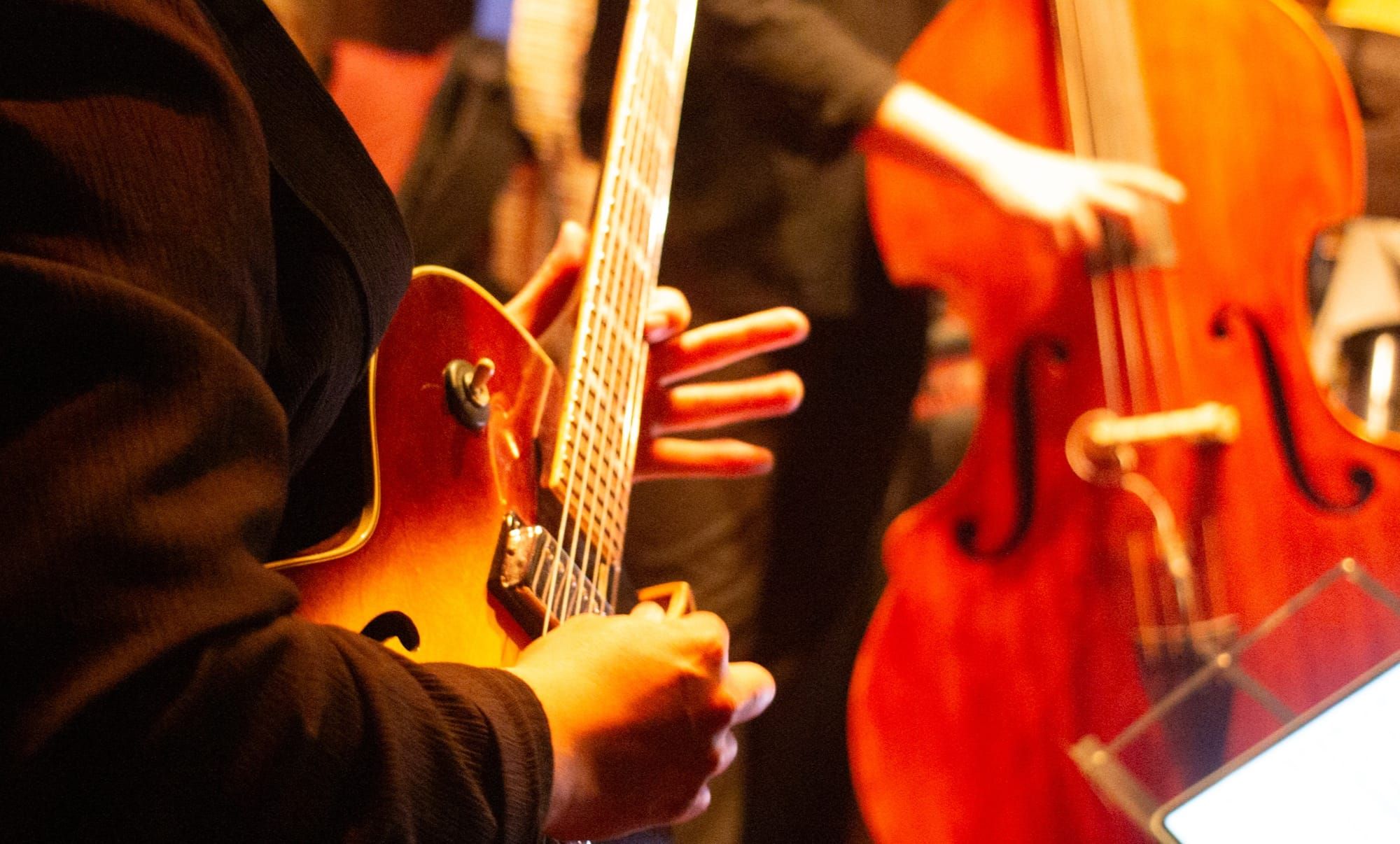 Close up of hands playing the guitar. Behind is a hand playing the bass.