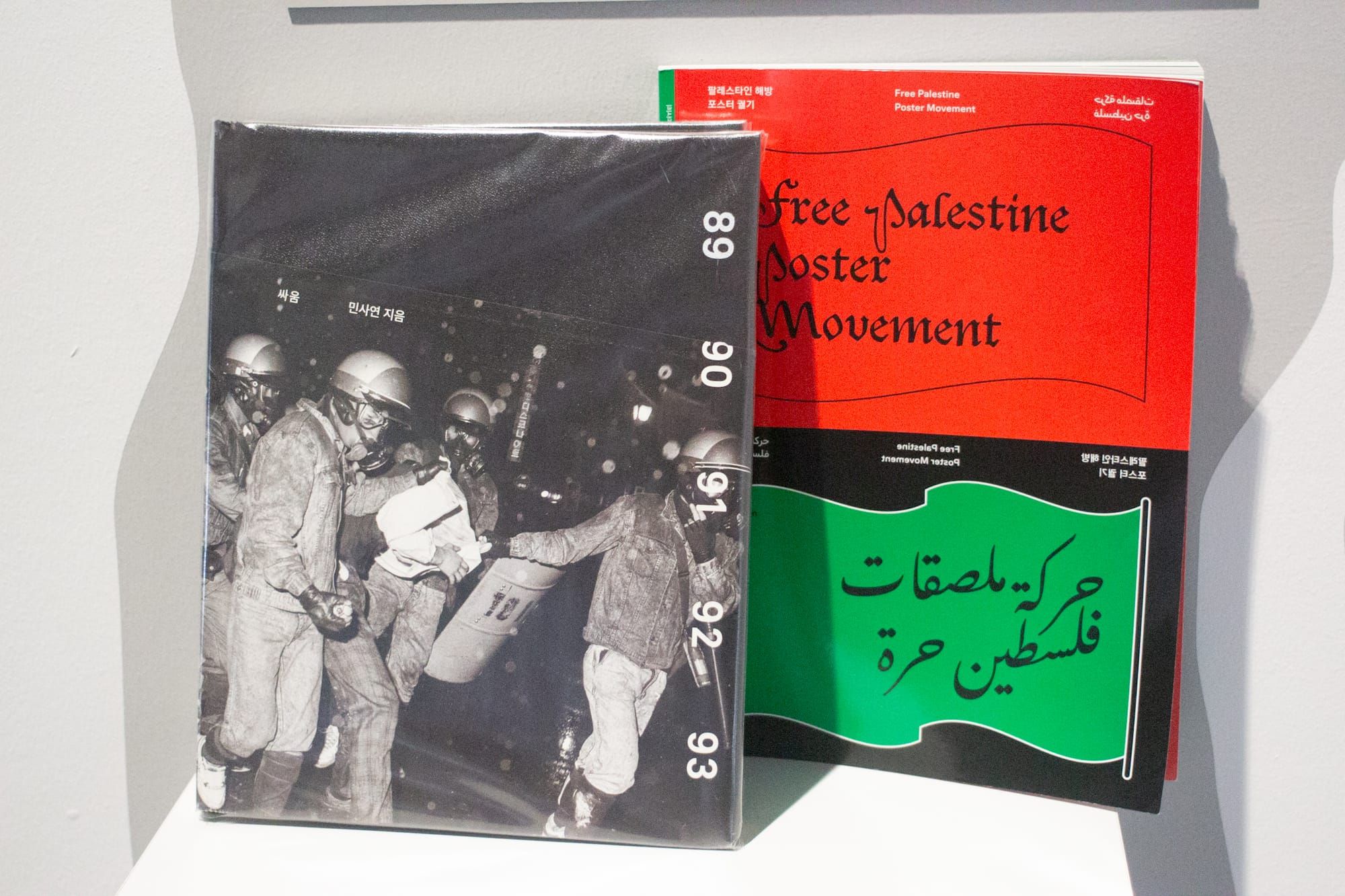 Two books side by side. One has a cover in black and white, a photo of cops dragging a protester. The other is red, green, and black sayinFree Palestine poster movement.