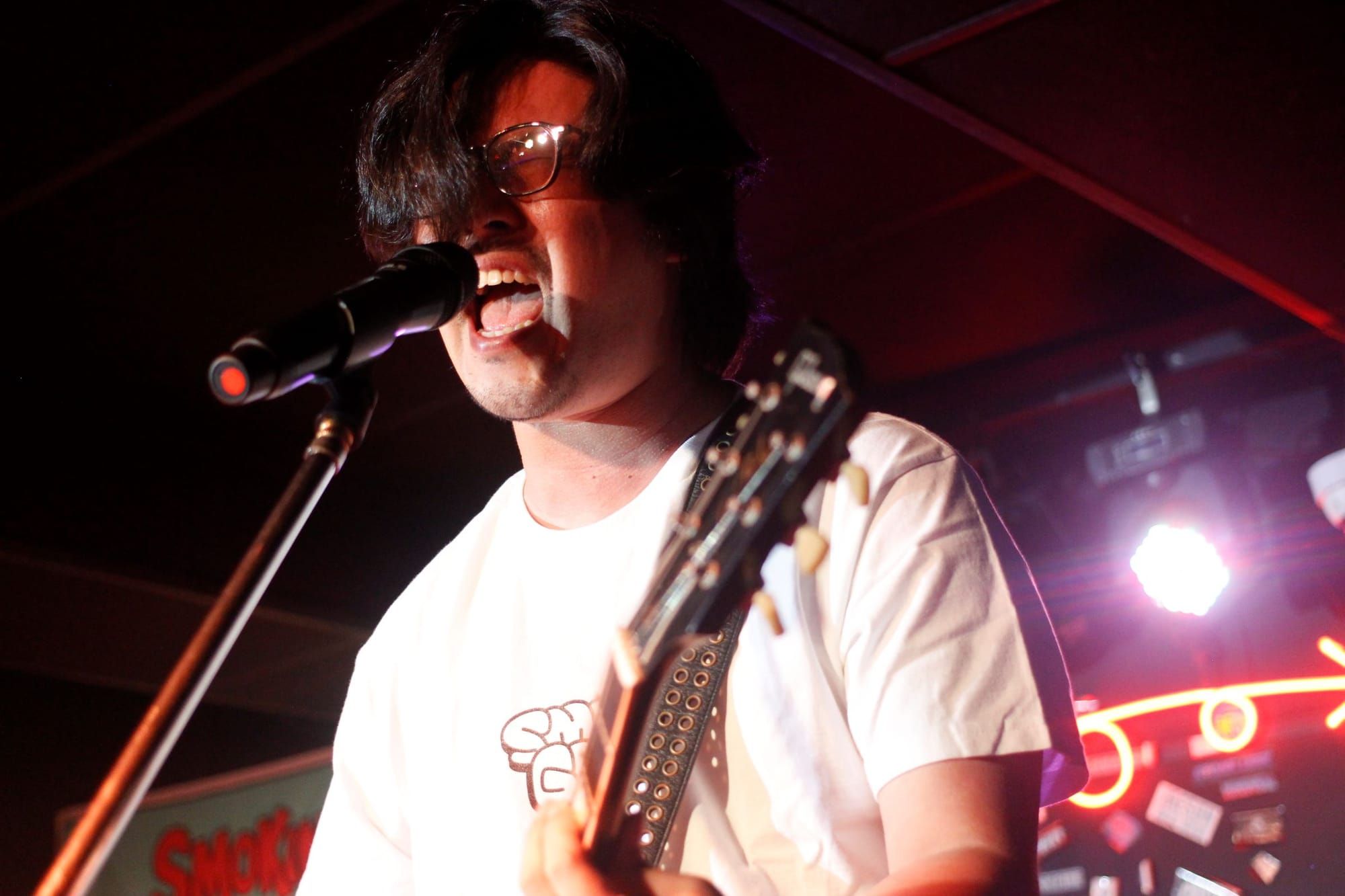 Kim Hee Jong scream-sings into the mic on stage, wearing a white shirt. You can see the letters SM and below that, G.