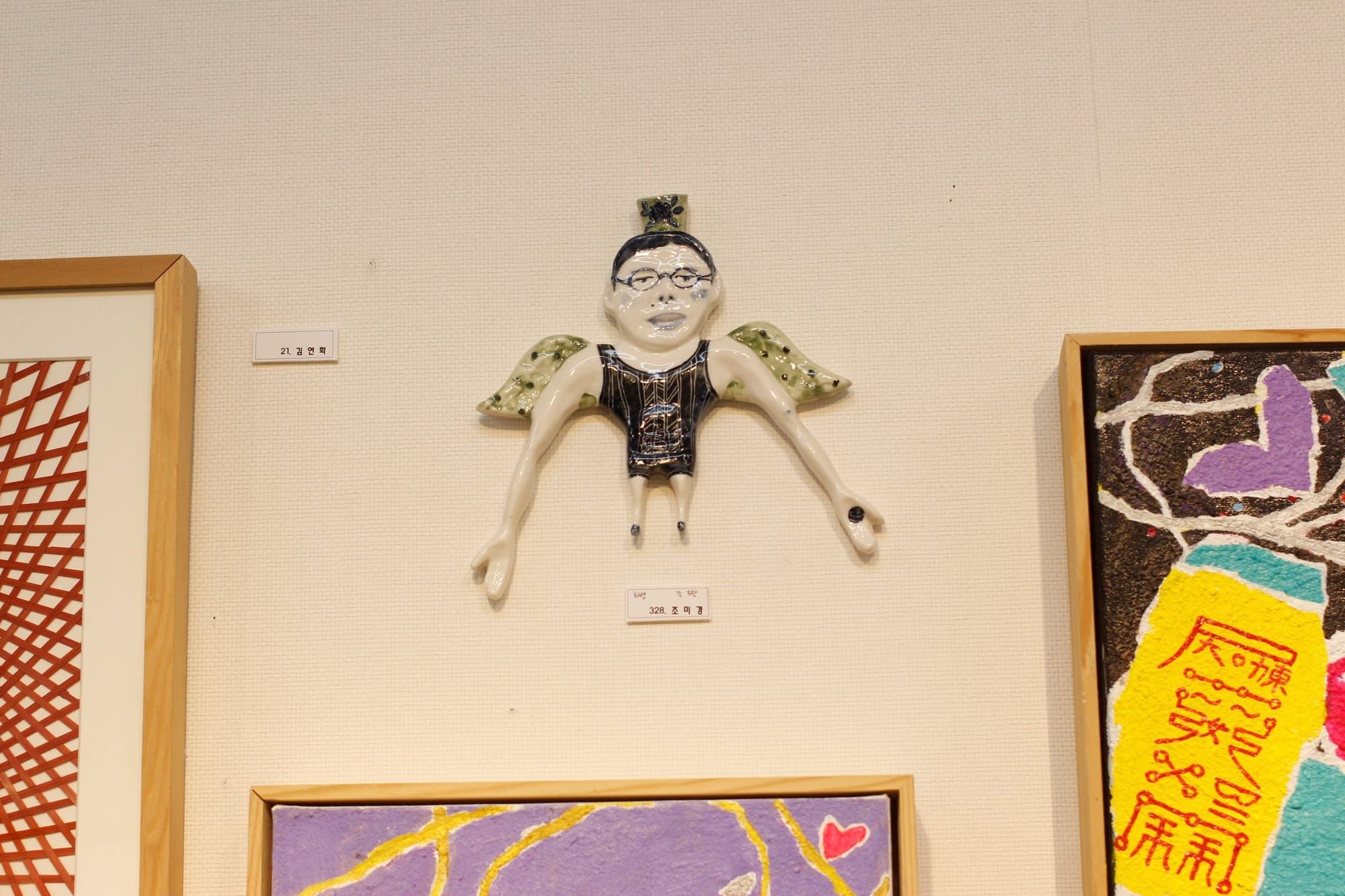 A ceramic wall hanging of a man with outstretched arms dangling lower than his legs is among 3 framed artworks.