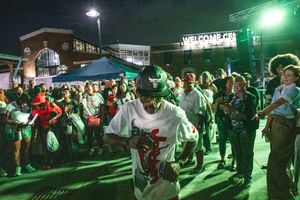 A man in a graphic t-shirt and cap dances under green lights at an outdoor night event.