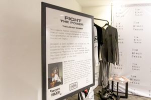 A white and black frame stands on an easel with the words “Fight the Power” a clothing rack and backdrop stands on the back. 