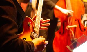 Close up of hands playing the guitar. Behind is a hand playing the bass.