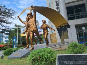 Larger than life-size bronze statue of three young adults running and shouting. They are carrying a long banner, which shows an illustration of a larger crowd.