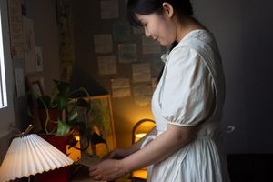 Seo Eun Ji, dressed in white, looks down at a desk with some lamps and plants.