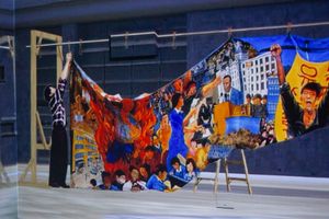 Somewhat blurry/aged image of a person in a flannel reaching up, pinning a loose painting to a rod resting on wooden supports. Many scenes centering people protesting.