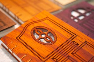 A close-up photo of a hand-bound notebook with a wooden cover in the shape of a door, with cutouts revealing white paper underneath.