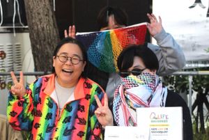 Three people close together, wearing rainbow colors and holding peace signs. The two younger ones have their faces partially covered.