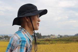 Yoon Hyung-Hyuk, wearing a hat with a brim, looks out over a yellow rice field.