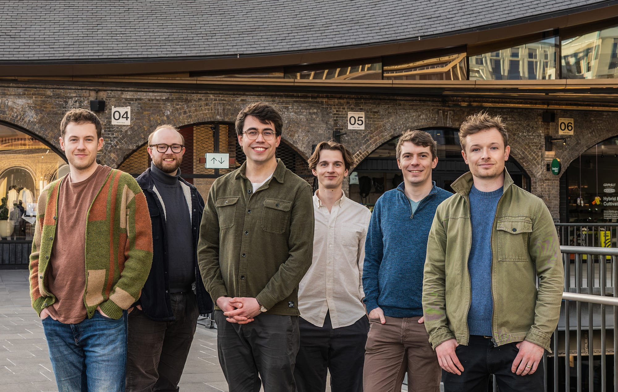 The Six, handsome male singers and fabulously casual attired pose in front of a modern urban building, serving harmony and collective cool.