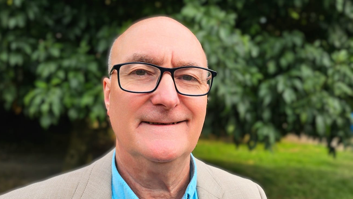 A portrait of John against a backdrop of green trees.