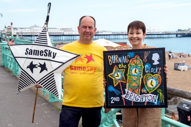 Caroline Lucas MP and John Varah holding a stamp on Brighton sea front