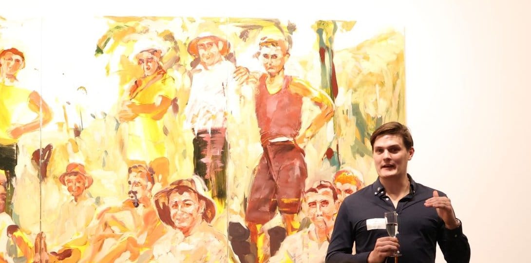 Sam Catlow presenting a Volary wine session in a gallery, glass in hand, in front of a large painting
