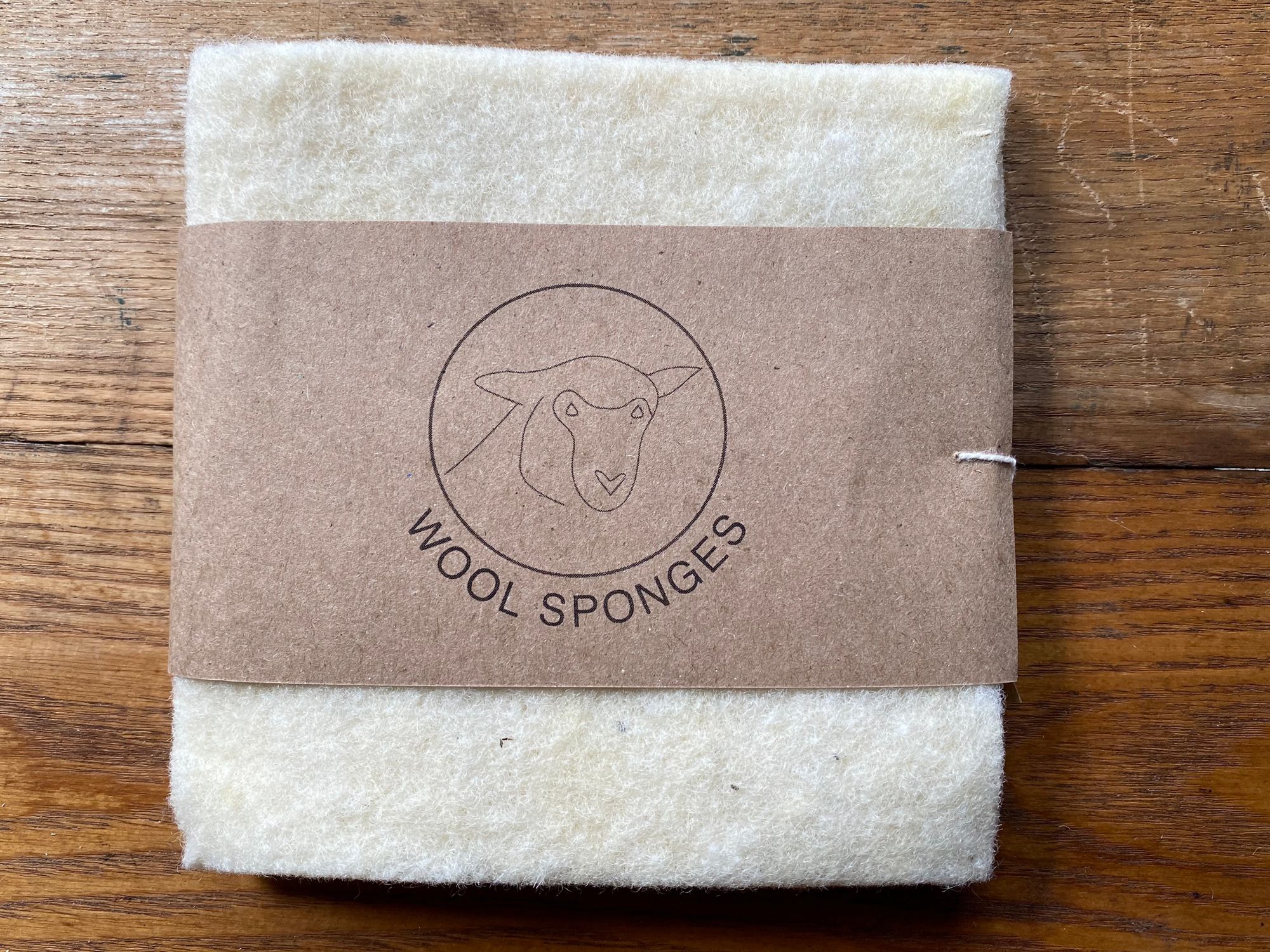 The Full Circle Wool Sponges, still in their plain brown paper packaging, sitting on a wool table.
