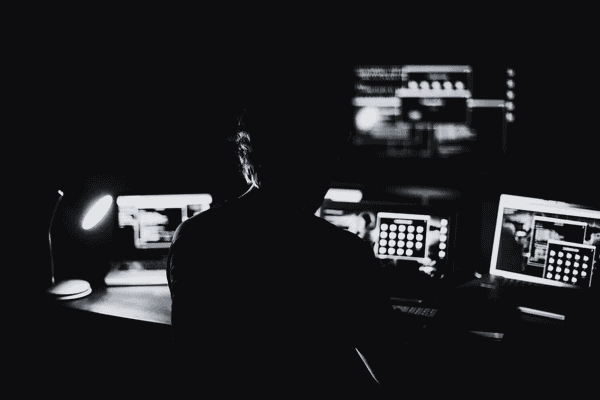 Silhouette of a person analyzing data on multiple computer screens in a dark room, symbolizing cyber investigation and digital forensics.