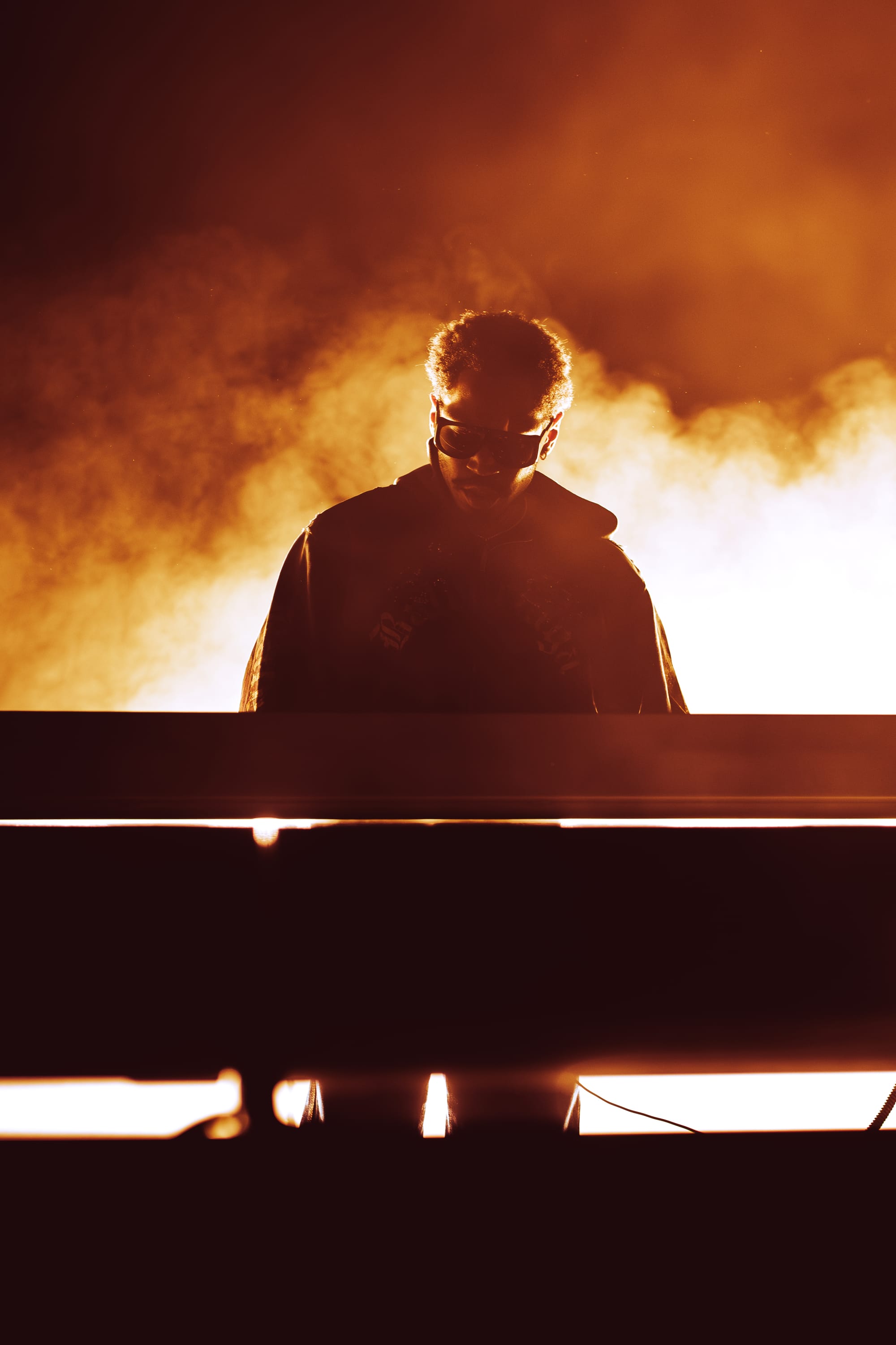 Kaytranada performing on stage at Co-op Live with a orange mist of light around him and DJ decks in front of him