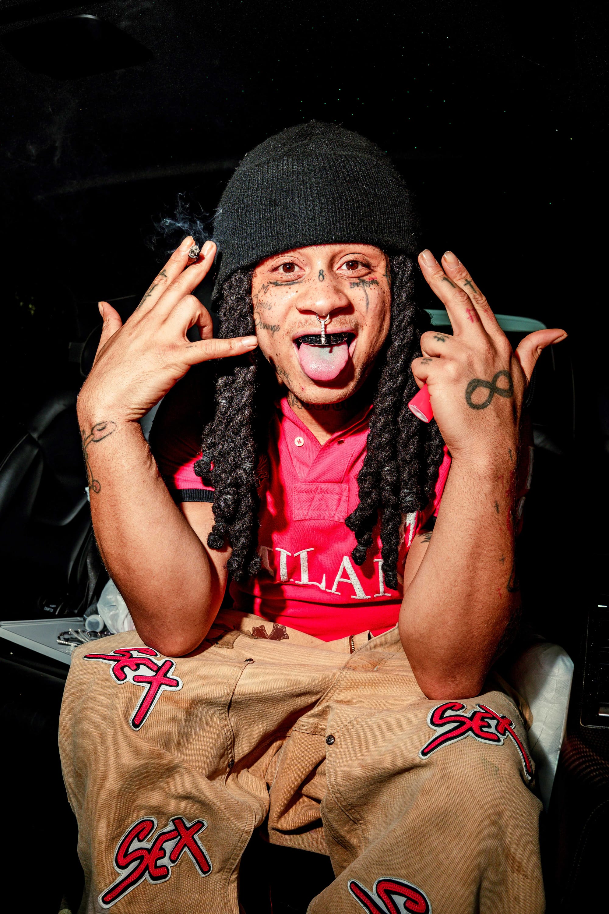 Trippie Redd at Leeds Festival 2025 throwing up hand signs wearing a pink shirt and beige trousers with 'sex' written on them